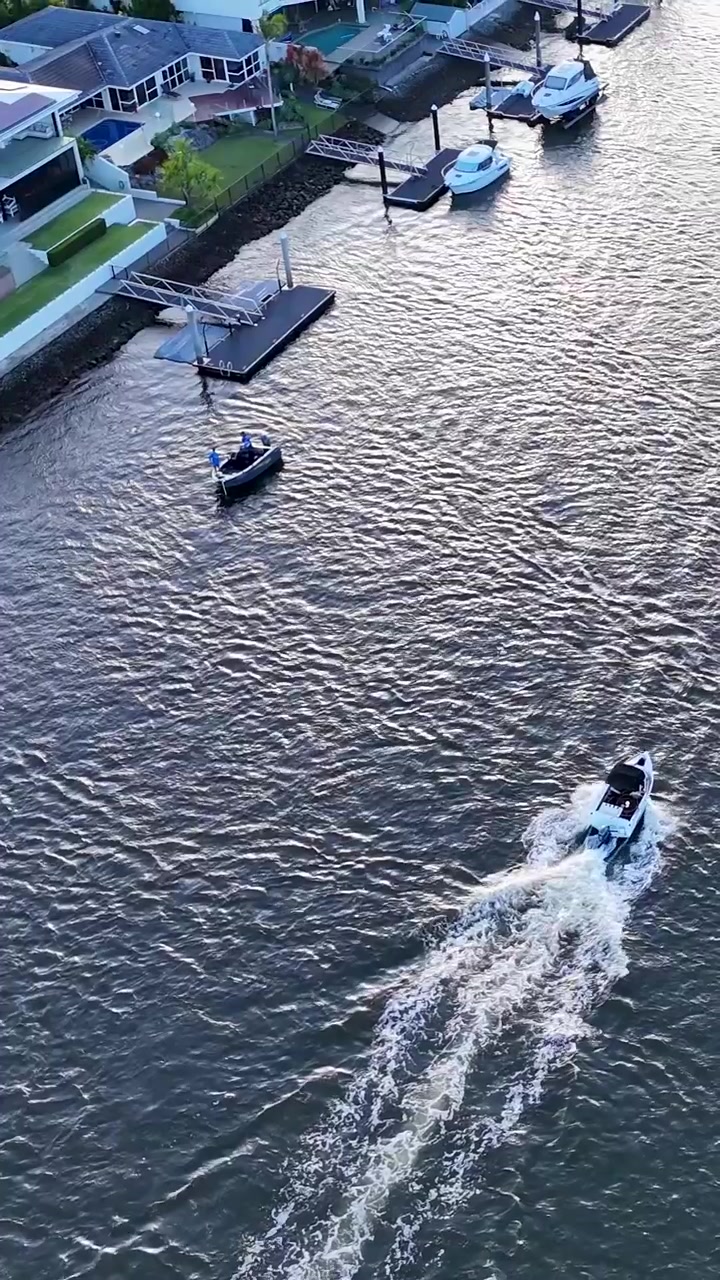 High angle drone shot of a boat creating a wake on a river near docks.