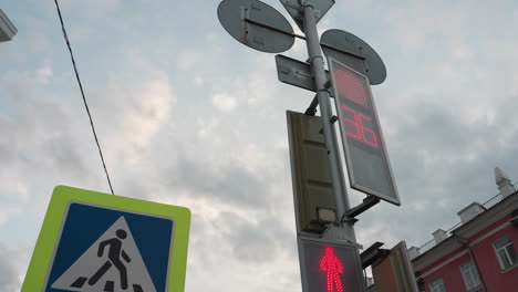 close view of a pedestrian crossing sign with a neon yellow border and a digital traffic light showing a countdown, with a building painted red by the side