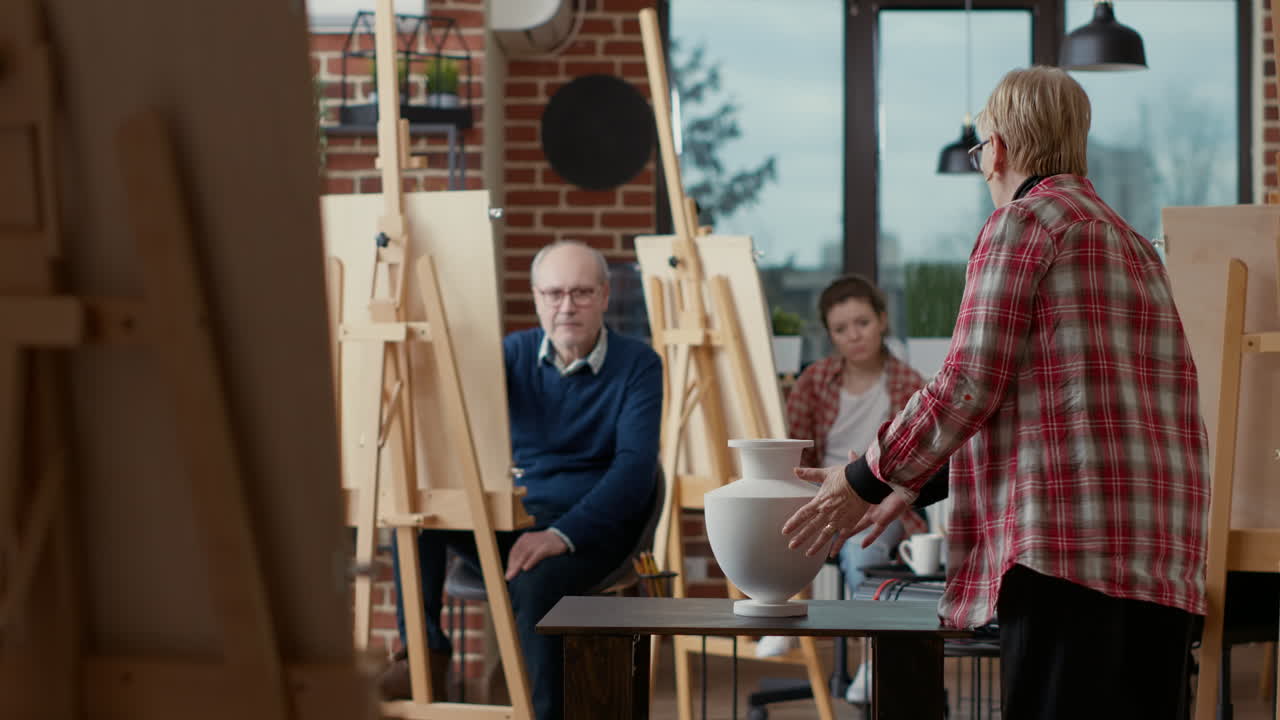 Elder artist pointing at vase on table to explain drawing technique