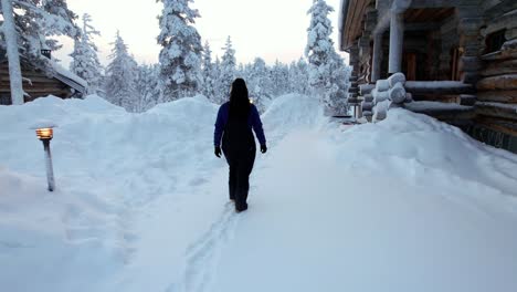 girl walking towards cabin in snowy winter wonderland in lapland, finland, arctic circle