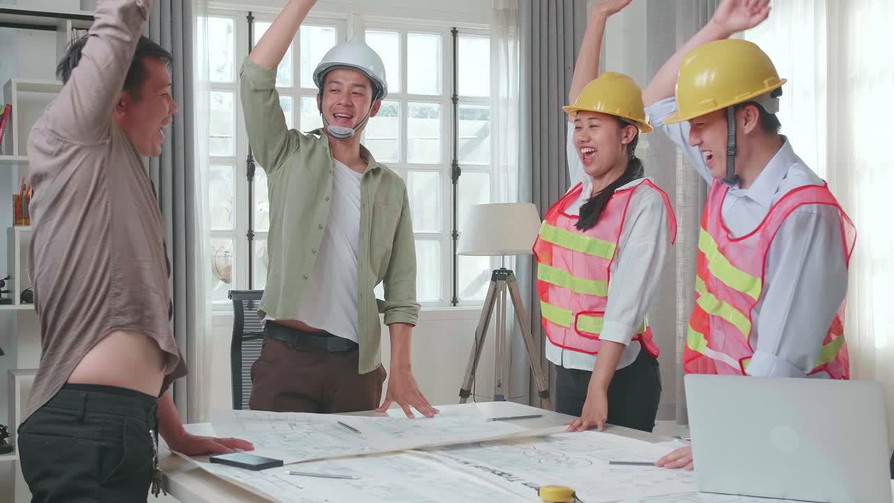 Three Asian Engineers With Helmets And A Man Celebrating Finish Drawing Building Construction While Working At The Office