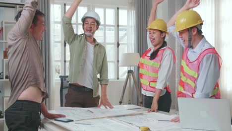 three asian engineers with helmets and a man celebrating finish drawing building construction while working at the office