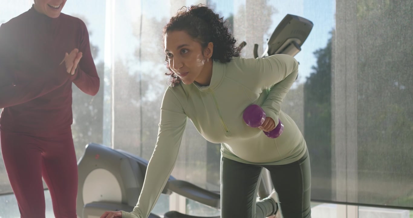 African American trainee doing single-arm rows with purple dumbbell on bench while trainer counting