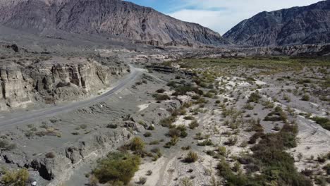 White-car-drives-on-mountain-highway-along-alpine-river-valley,-aerial