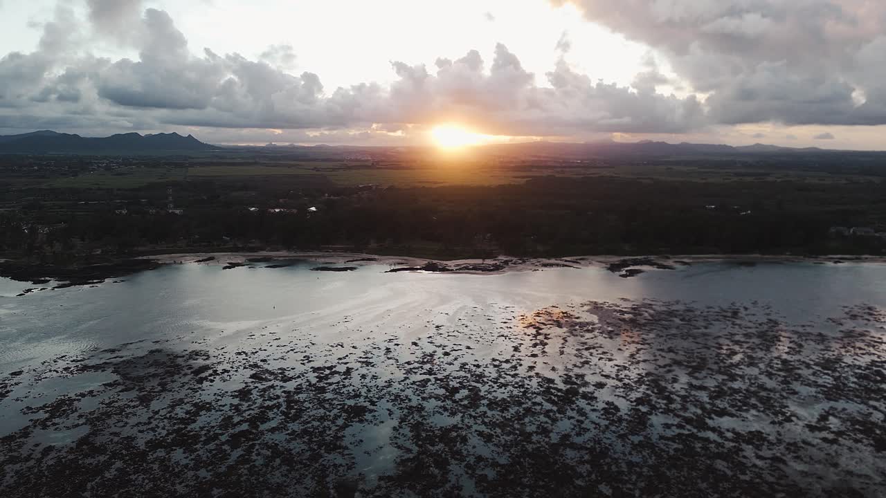 Luchtfoto van zonsondergang boven Belle Mare Beach bij eb op Mauritius, met gouden reflecties, wolken en een kalme kustlijn. Concept van rust, het verstrijken van de tijd en serene kust.