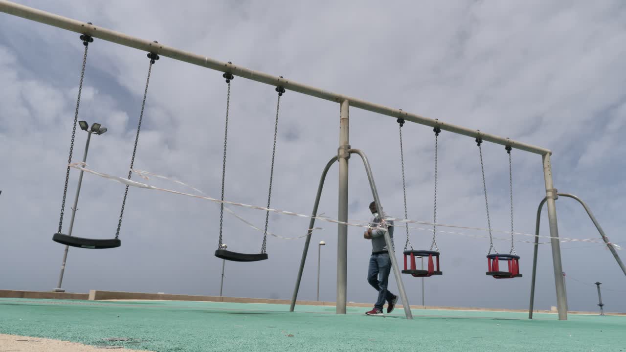 Man in face mask pass through empty closed playground, coronavirus pandemic