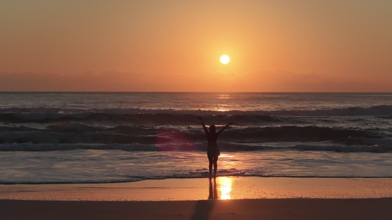 Vista aerea con drone di una persona che cammina su una spiaggia sabbiosa all'alba con un grande sole arancione all'orizzonte