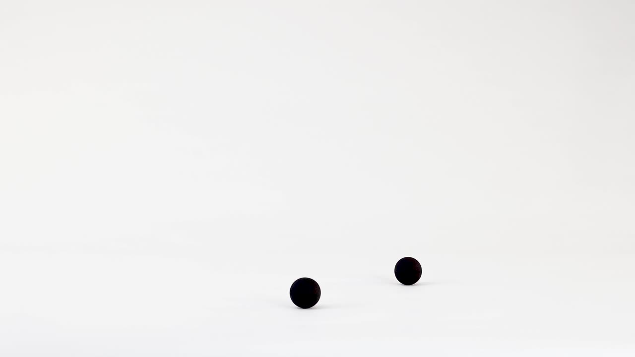 Small black spheres drop from above, bouncing and rolling across a clean white minimalist surface