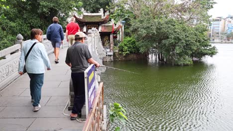 people walking on bridge near temple and lake