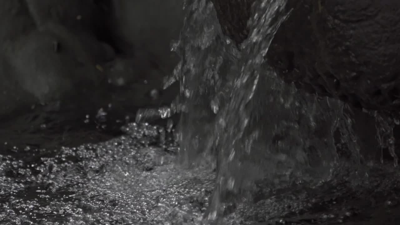 A close-up of a natural waterfall cascading over smooth, tiered limestone rock formations, creating a series of small pools in the dense Chiapas jungle