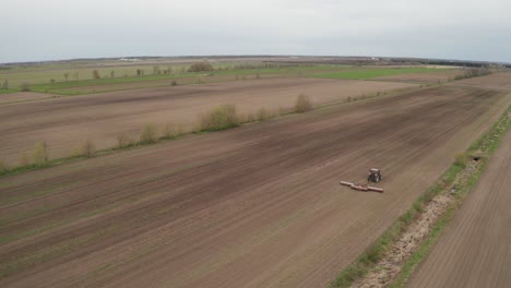 Overhead-view-from-drone-tracking-tractor-tilling-field-to-prepare-soil-for-planting-new-crop-on-large-farm-with-long-flat-fields