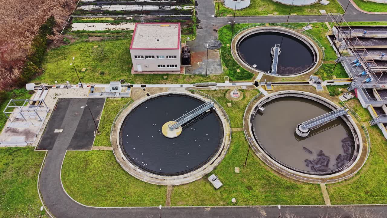Workers manage a wastewater treatment facility with tanks and buildings