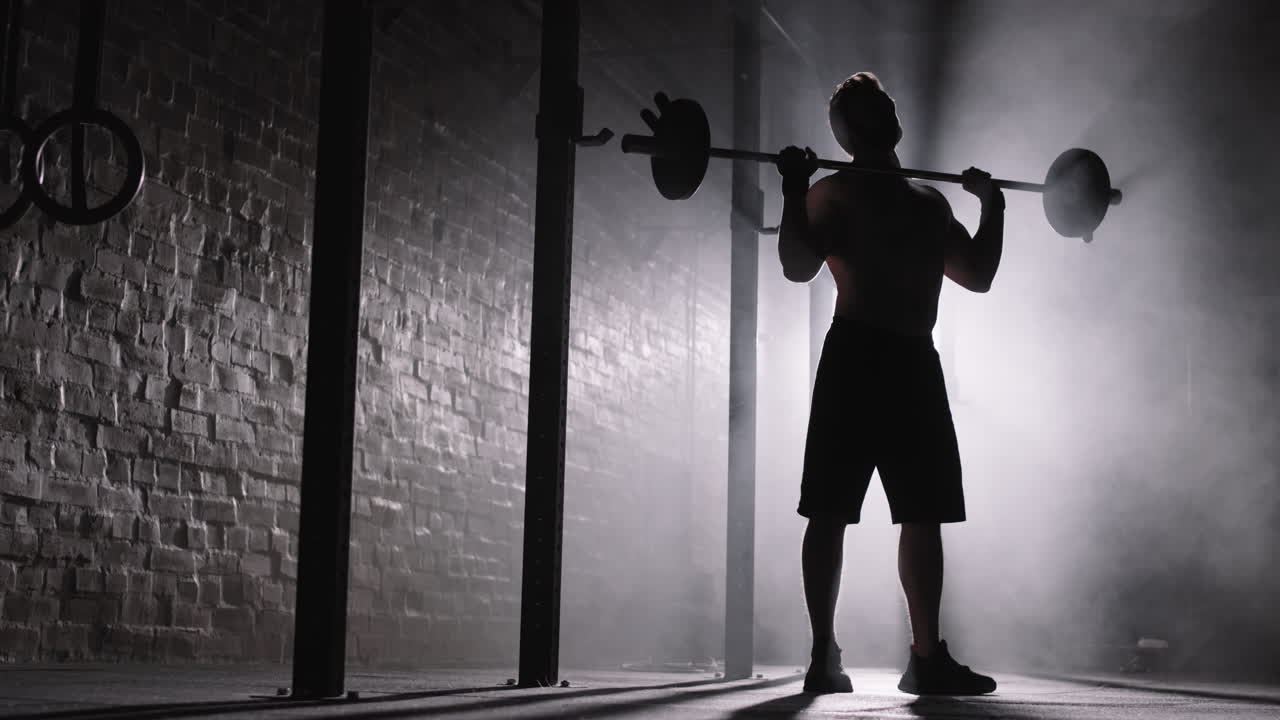 Silhouette of Sportsman Lifting Barbell in Darkness