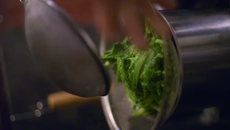 Green-leafy-vegetables-moved-from-one-metal-strainer-into-another-metal-strainer-for-draining-water,-filmed-as-vertical-closeup-slow-motion-shot