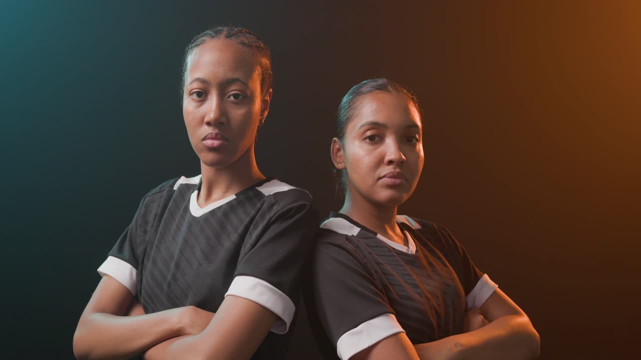 African women in dark kits crossing arms on crop leaning back-to-back showing power under teal rim