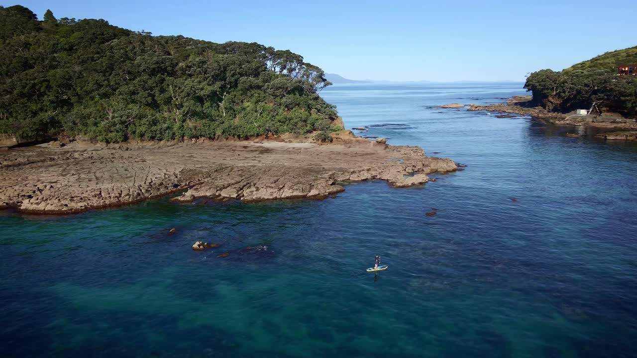 Wide Circle Aerial Shot Around Man On Paddle Board Crossing Goat Island Marine Reserve Calm Sea Channel, New Zealand