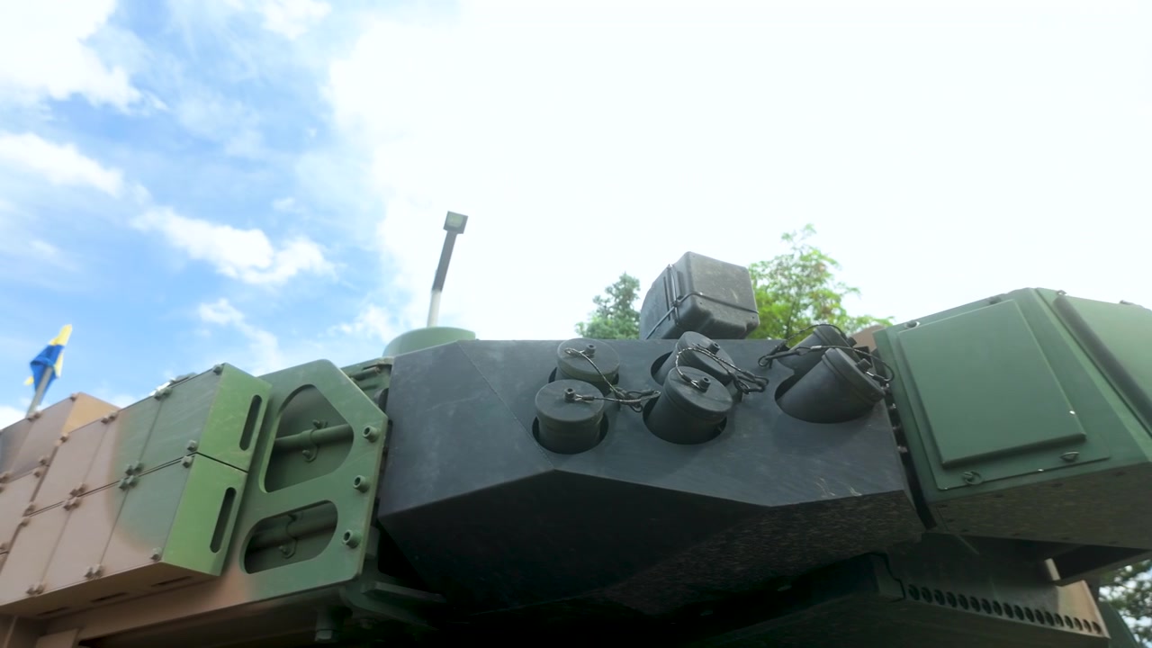 Vue en contre-plongée d'une tourelle de char de combat principal moderne, dotée d'un blindage réactif et de lance-grenades fumigènes, sous un ciel bleu. Convient pour le contenu sur la défense, la sécurité et la technologie militaire.
