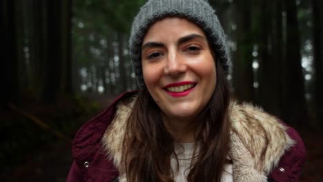 Primer-Plano-De-Una-Mujer-Sonriente-En-Un-Bosque-Oscuro-Usando-Un-Gorro-Para-El-Frío