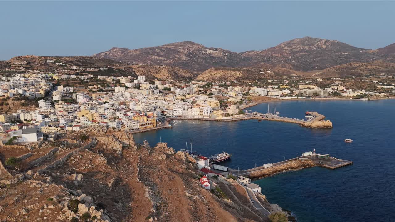High drone footage revealing the vibrant port of Pigadia, Karpathos, with ferries, boats, and stunning coastal views under clear skies in the heart of the Dodecanese islands