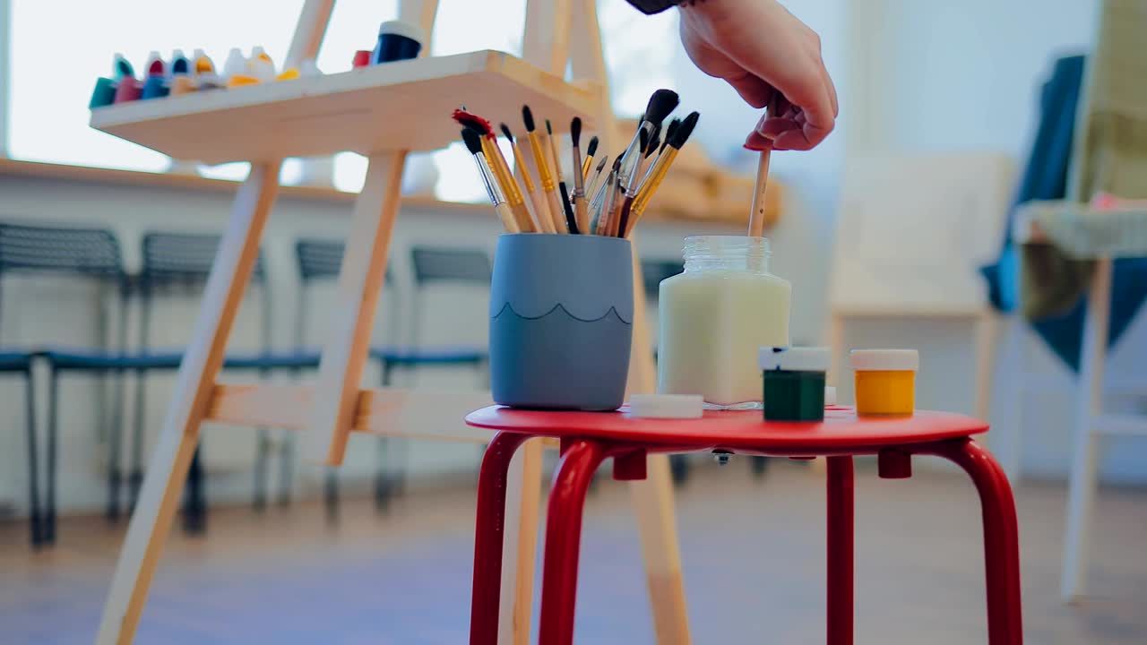 el artista sumerge el pincel en un frasco de agua. lugar de trabajo del artista. movimiento circular de la cámara.