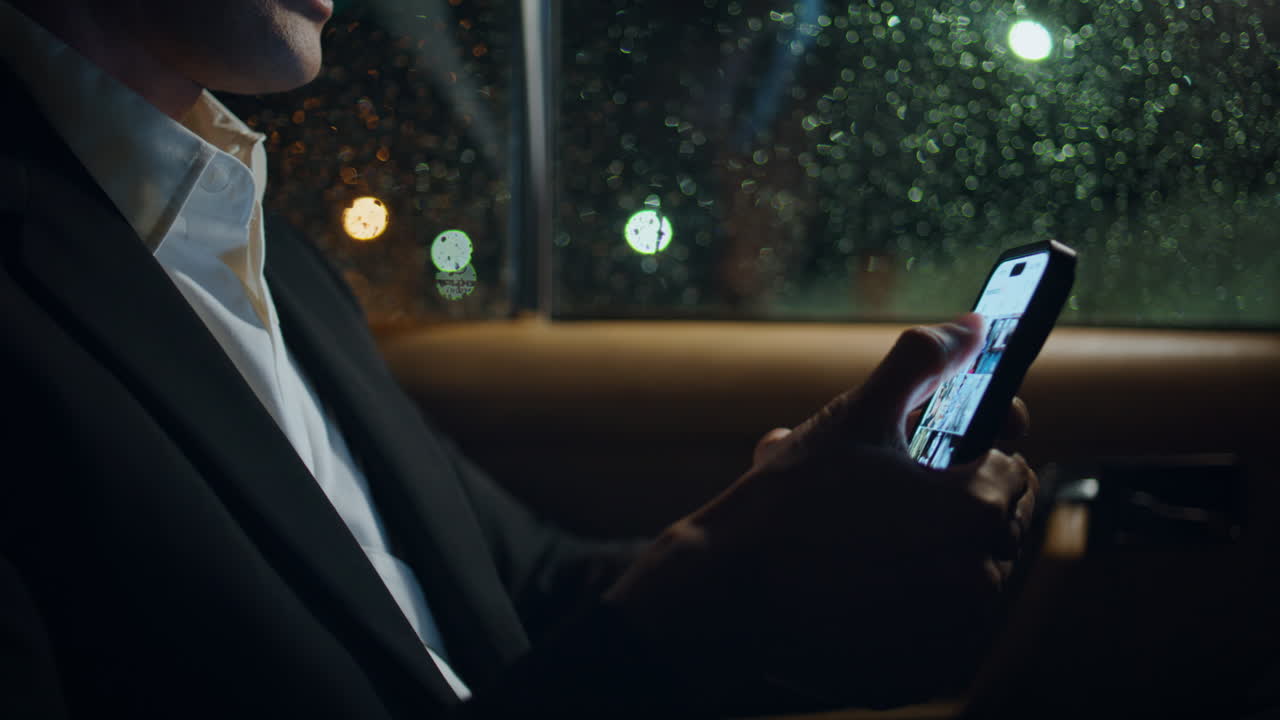 Man fingers swiping phone in evening rainy auto close up. Boss holding cellphone