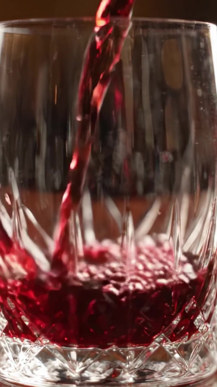 Una trasformazione in primo piano: da un bicchiere di cristallo vuoto a un bicchiere pieno di ricco vino rosso, affascinante su una superficie di legno scuro.