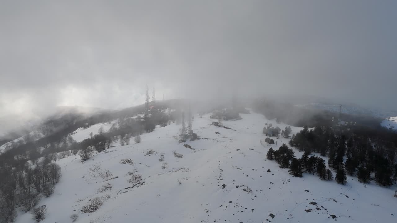 무거운 안개 구름이 tv 기둥과 함께 숲과 눈 인 산꼭대기에 떠다니고 있습니다.
