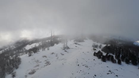 nubes de niebla pesadas flotando sobre la cima de la montaña nevada boscosa con mástiles de televisión