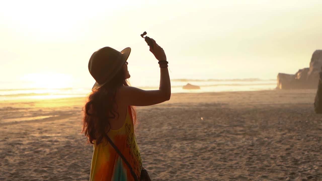 woman at beach at sunset filming with a gimbal. slow motion