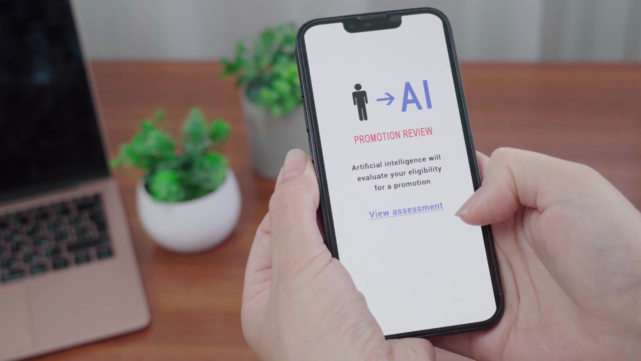 Person holds a smartphone showing an AI promotion review message on screen at a tidy office desk.