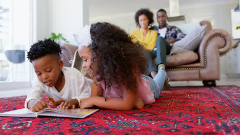 Vista-Frontal-De-Lindos-Niños-Negros-Leyendo-Un-Libro-De-Cuentos-En-La-Sala-De-Estar-De-Una-Cómoda-Casa-4k