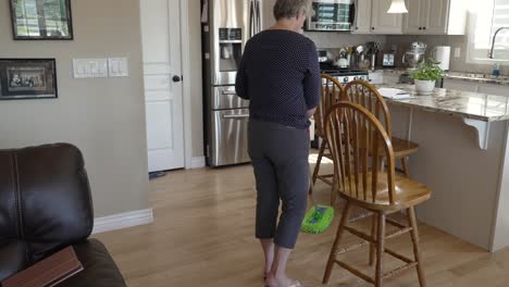 Mujer-Mayor-Limpiando-Sus-Pisos-De-Cocina-De-Madera-Dura---Incline-Hacia-Abajo