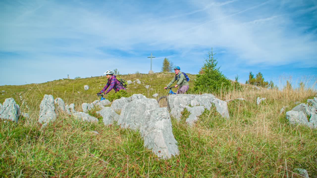 Снятый с нижнего угла кадр, на котором два молодых и активных горных байкера спускаются по склону
