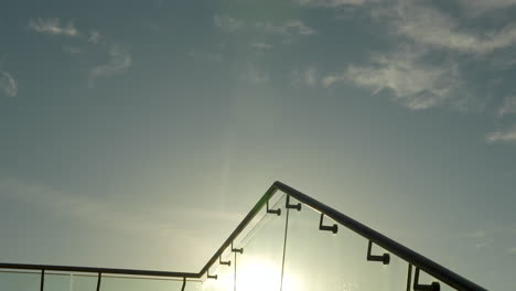 sun shining through a sleek glass railing, silhouette of masts in the background