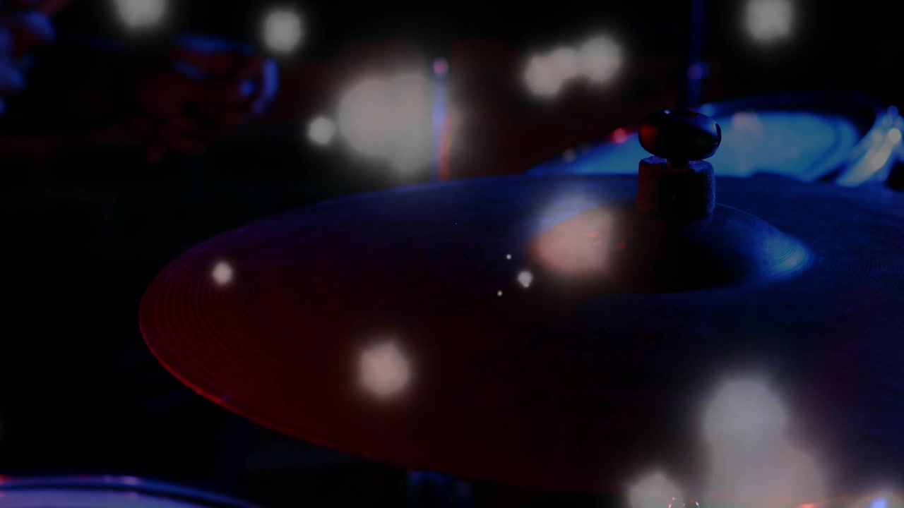 Bacchetta che colpisce il piatto, mani che creano un luccichio durante il concerto, sfere bokeh rosse e blu che evidenziano la curvatura.