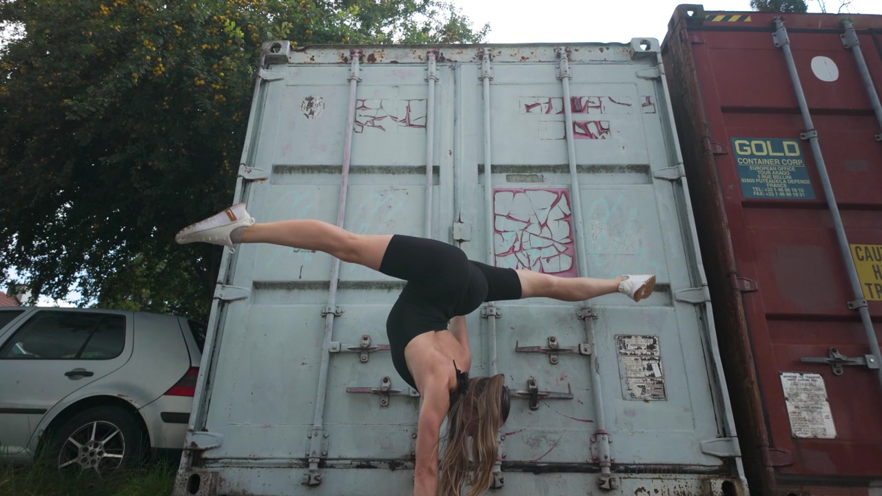 Athletic caucasian girl doing handstand pose on shipping a container