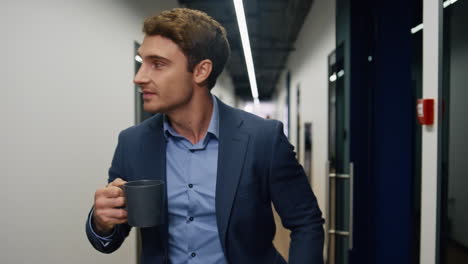 empleado relajado sosteniendo una taza de café de cerca. ceo de la compañía caminando por el pasillo descansando
