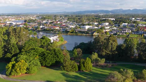 drone footage captures lush greenery, suburban houses, and a winding river under bright daylight in gold coast, australia