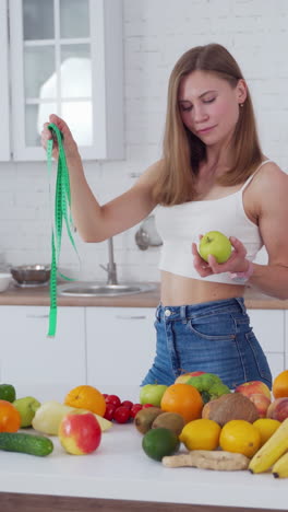 sporty woman standing near fruits. happy young woman with muscular body standing in the kitchen. vertical video