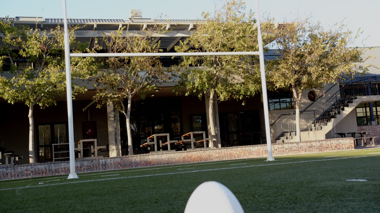 Rugby ball on field with goalposts in background, ready for kick-off, copy space