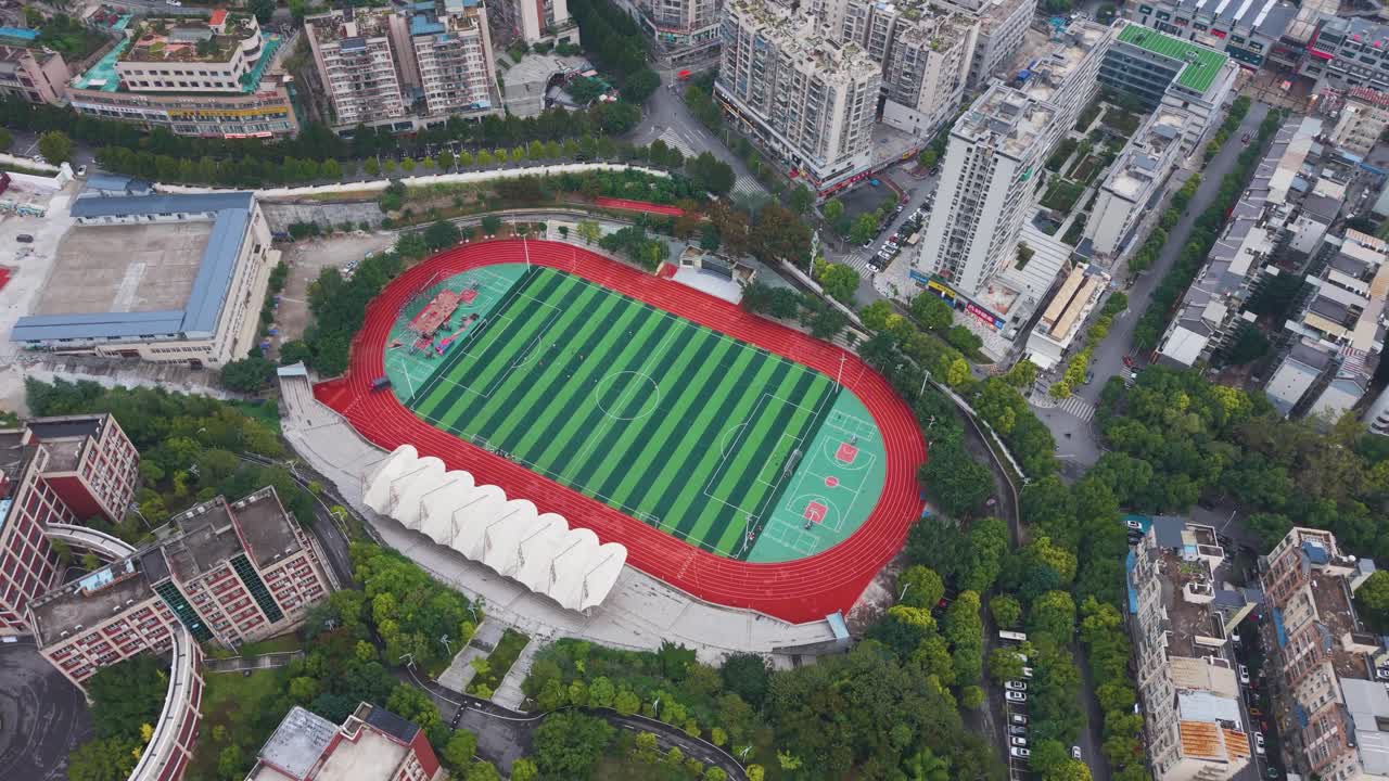 Aerial shot of a vibrant sports stadium in Wuxi City, showcasing a green athletic field, red running track, and surrounding urban landscape. Sports, education, and cityscape projects. China, UHD