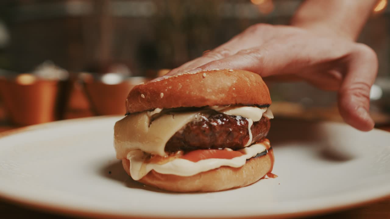 primer plano de una hamburguesa fresca y jugosa, exprimida por las manos del chef