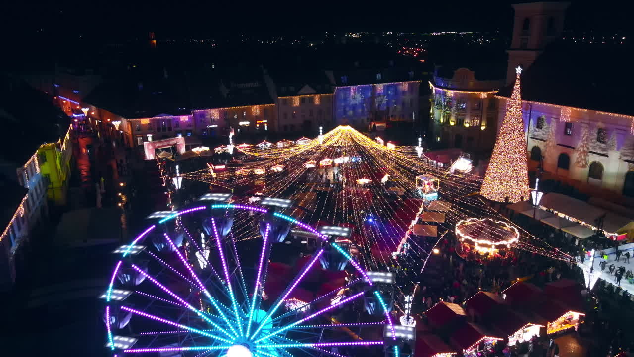Aerial drone view of The Big Square in Sibiu at night, Romania. Old city centre decorated for Christmas. Ferris wheel, skating rink, people
