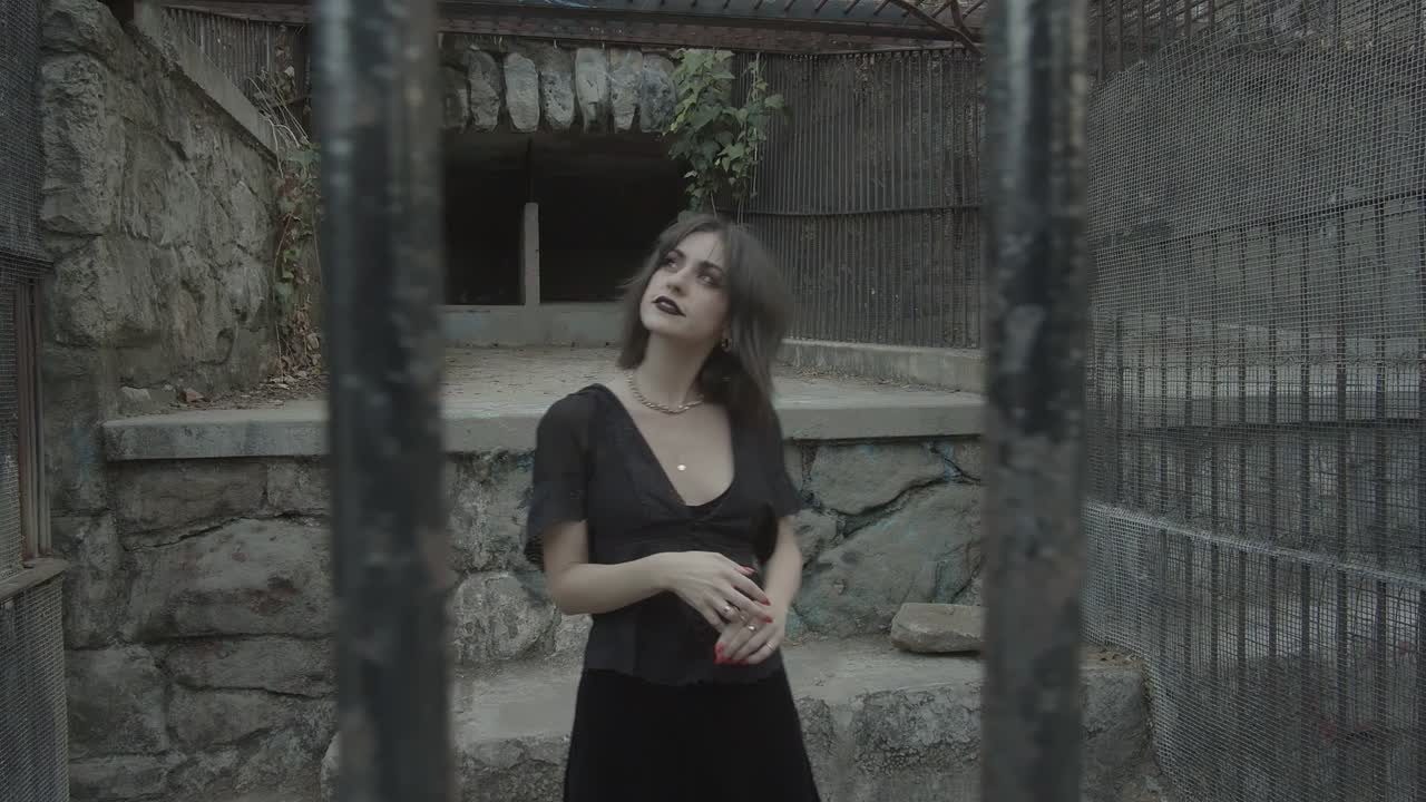 Junges Mädchen posiert in einem schwarzen Kleid, in einer Zelle gefangen, Blick durch Gefängnisgitter
