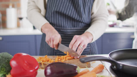sección media de la mujer con delantal cortando verduras en la cocina en casa