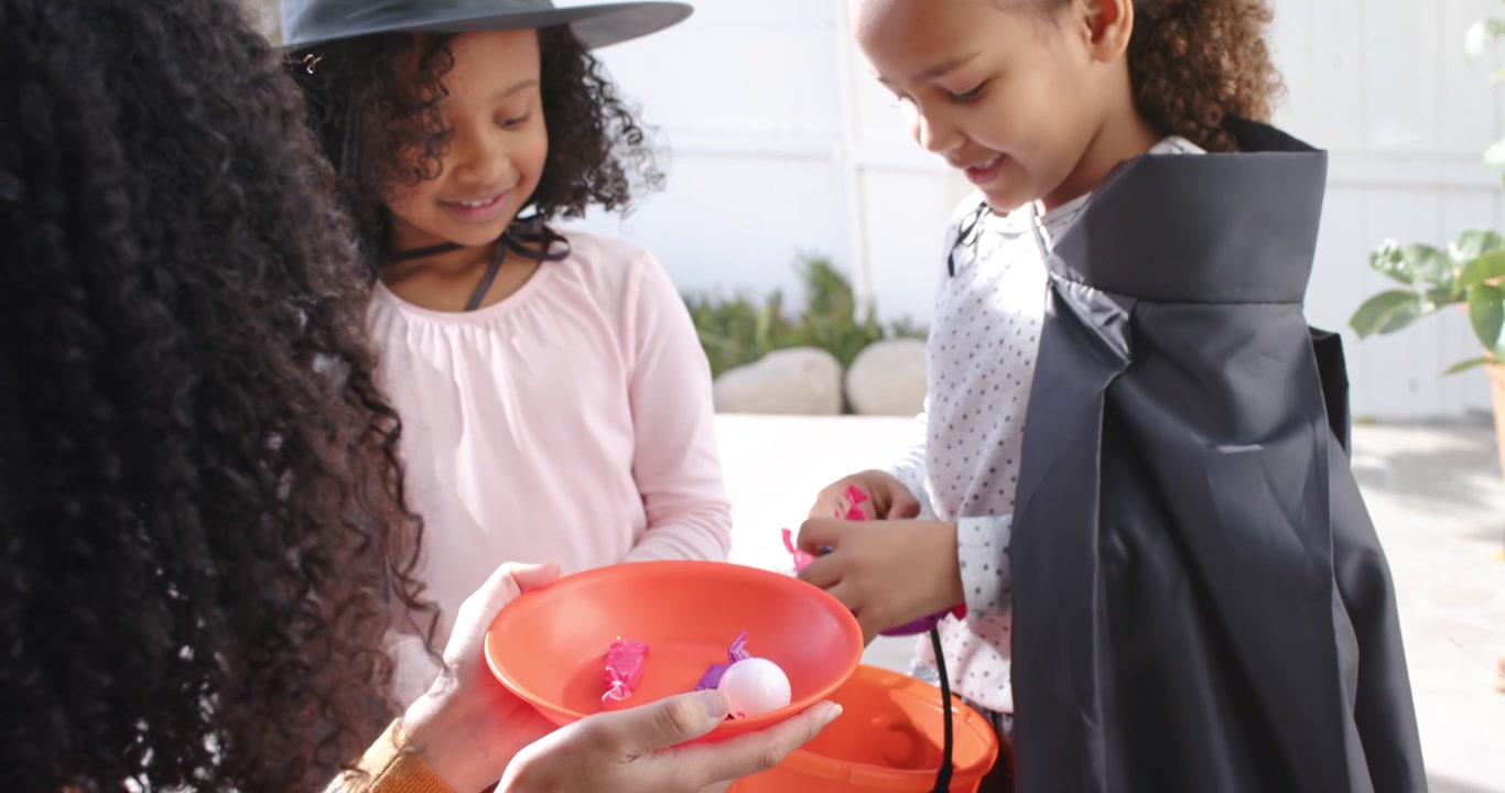ハロウィンのカボチャにボウルからキャンディをもらうアフリカ系アメリカ人の少女たちと世話人