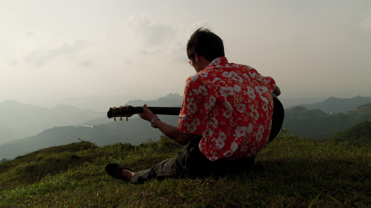 Güzel doğada, bir tepede akşam melteminin tadını çıkararak gitar çalan erkek.