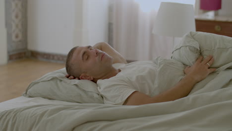 caucasian man sleeping on back in bed with hand behind head