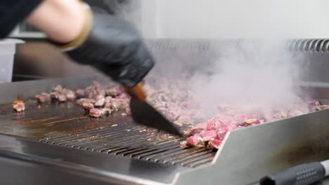 chefs hands grilling meat strips on professional grill