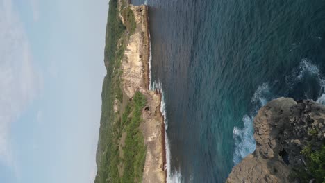 vertical format aerial rises over seaside cliffs and azure ocean water